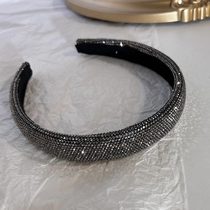 Dettaglio di un cerchietto largo con strass grigio scuro scintillanti su base nera lucida