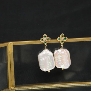 Detail of baroque pearl earrings with green gemstones and golden flower base setting