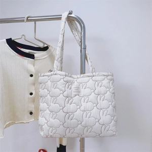 Detail of white quilted tote bag featuring red rabbit embroidery and elegant fabric label