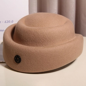 Detailed close-up of camel wool stewardess hat with elegant metallic M letter emblem
