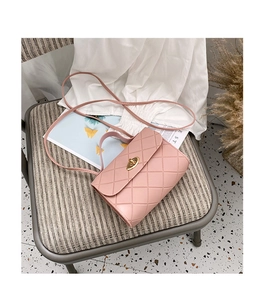 Pink quilted crossbody bag with gold twist lock on a cozy fabric chair detail