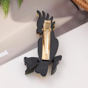 Detail of a black parrot acrylic hair clip featuring a golden metal duckbill clasp back