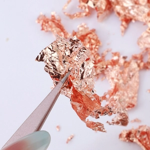 Macro shot of rose gold metallic flakes for nail art and crafts with tweezers detail