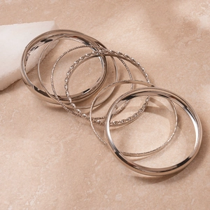 Detailed macro view of 8-piece silver metal bangles set on textured stone surface