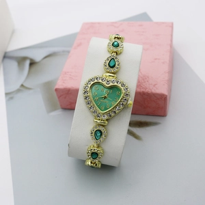 Détail d'une montre coeur dorée avec pierres vertes dans un coffret rose