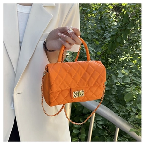 Detail of orange quilted handbag with gold chain strap held by a model in a white blazer