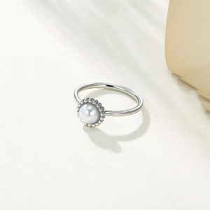 Macro shot of silver stainless steel ring featuring a central white pearl on stone