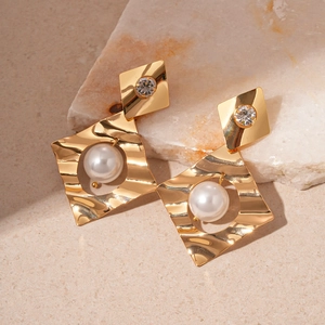 Detail of gold geometric earrings with pearls and crystals on a stone prop