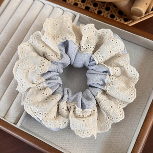 Detailed close-up of a layered floral lace scrunchie with beige embroidery and silver fabric