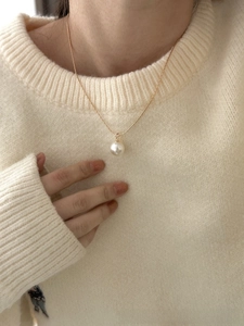 Elegant single white pearl pendant on a delicate gold snake chain worn over a beige sweater