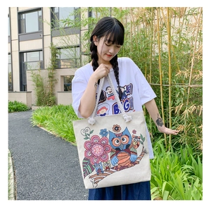 Detailed close-up of colorful owl and floral embroidery on cream canvas tote bag