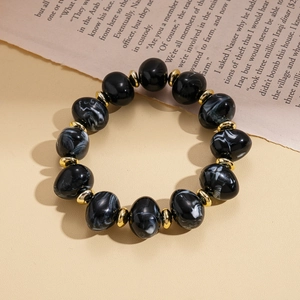 Close-up of black marble acrylic beads with golden metal spacers on vintage newspaper