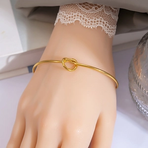 Detail of a minimalist gold knot open cuff bracelet worn with a lace cuff and glass