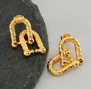 Macro detail of gold horseshoe earrings with hammered texture and double-U interlocking design
