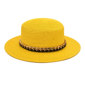 Détail d'un chapeau de paille jaune à calotte plate avec chaîne dorée et cordon noir