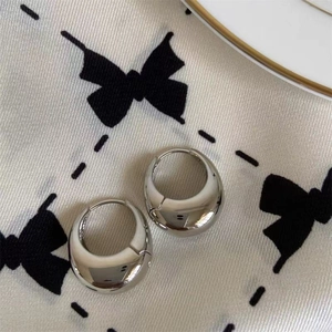 Detailed close-up of polished silver C-shaped hoop earrings on elegant silk fabric
