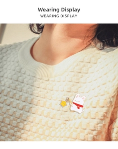 Detailed view of a cute white rabbit enamel pin with a red scarf on a white knit sweater