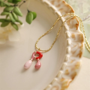 Détail d'un collier chaîne dorée avec pendentifs en émail rose et rouge sur un plat en céramique