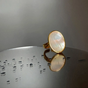 Close-up of golden oval ring with iridescent shell inlay reflecting on a wet surface