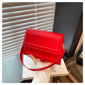 Close-up of a stylish red leather crossbody bag held by a model in soft window light