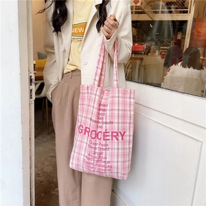 Close-up of pink checkered canvas tote bag with red Grocery typography in a cafe setting