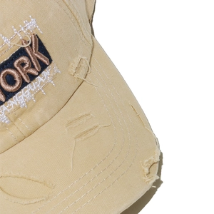 Detail of New York embroidery and distressed ripped brim on a khaki cotton baseball cap