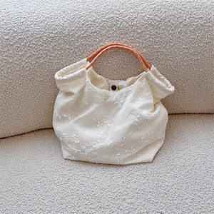 Detail of floral embroidery on off-white canvas tote bag with orange rope handle