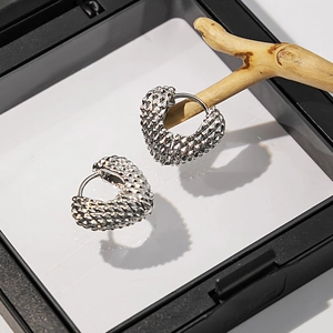 Vue macro de la boucle d'oreille cœur argentée avec texture diamant 3D sur support bois