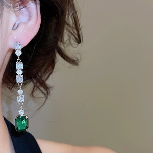 Close-up of dangling silver earrings with square zircon and large emerald green gemstone