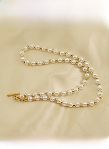 Détail d'un collier de perles blanches avec billes dorées et un fermoir à bascule OT