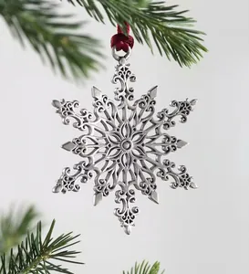 Detailed snowflake metal pendant with engraving and red ribbon on green pine branch