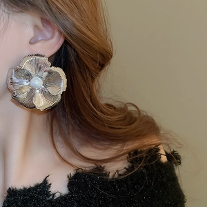 Close-up of metallic silver flower stud earrings with a pearl center on model's ear