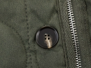 Detail of army green twill fabric featuring dark coffee resin button and metal zipper close-up
