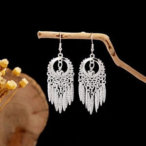 Detailed view of silver ethnic leaf earrings with tassels hanging on a wooden branch