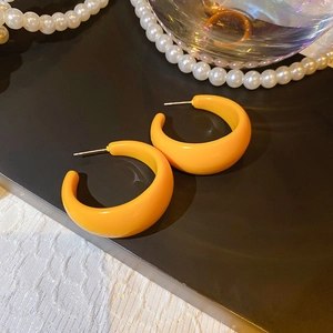 Detailed view of glossy orange C-shape earrings with silver needles and pearl decor