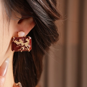 Detail of red enamel square earring with gold floral relief and pink gemstone on model
