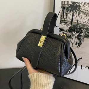 Handheld view of black textured leather handbag with vintage gold clasp and top handle