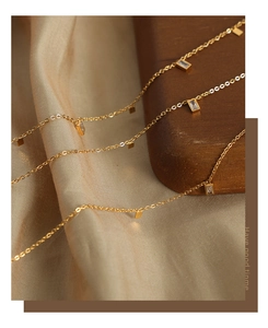 Detail of a gold titanium necklace featuring small rectangular pendants with zircon stones