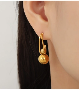 Close-up of a double geometric gold ball drop earring worn by a model in soft light