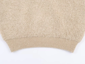 Détail de la texture en maille bouclée beige et de l'ourlet côtelé sur ce haut douillet