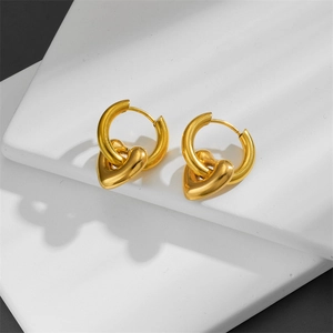 Polished 18K gold heart huggie earrings displayed on a minimalist geometric pedestal