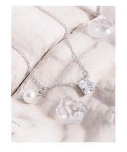 Detail of silver S925 necklace with white pearl and square zircon on a stone surface