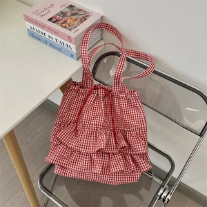 Detail of red gingham ruffle tote bag with drawstring on a modern transparent chair