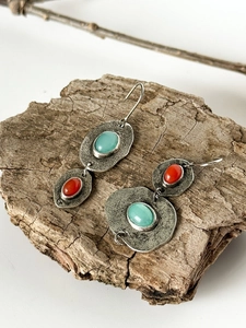 Detalle de pendientes bohemios de plata con piedras azules y coral sobre corteza natural