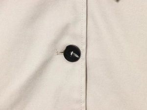 Dettaglio del tessuto beige di un trench con bottone nero e cuciture di precisione