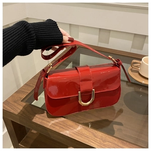Close-up of red patent leather bag featuring a gold horseshoe buckle and adjustable strap