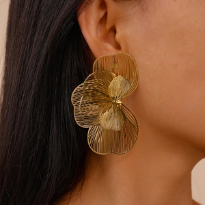 Close-up of oversized hollow metal flower earring in gold finish on a model