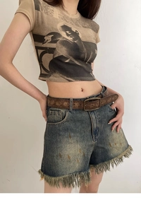 Detail of dark brown embossed leather belt with bronze buckle on distressed denim shorts