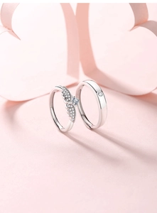 Detailed close-up of S925 sterling silver angel wing couple rings on a romantic pink backdrop