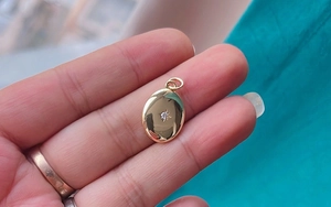 Close-up of a golden oval pendant with a star cutout and sparkling stone on a hand